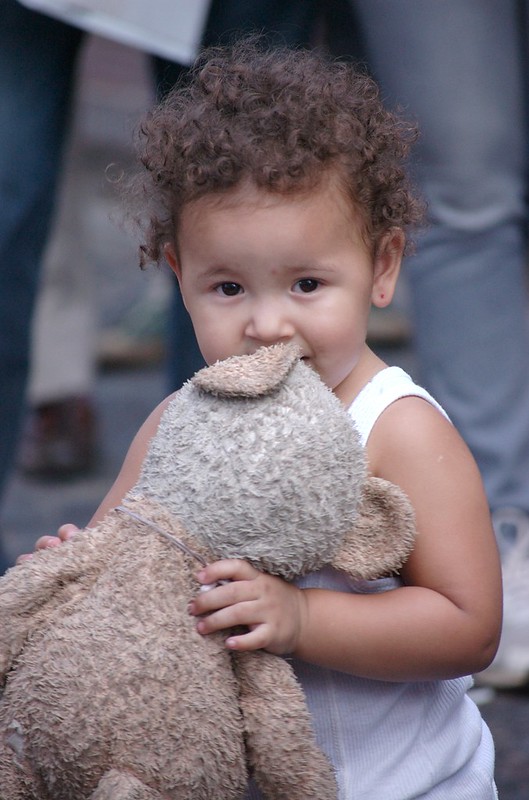 Curly-haired toddler holding a well-loved teddy bear