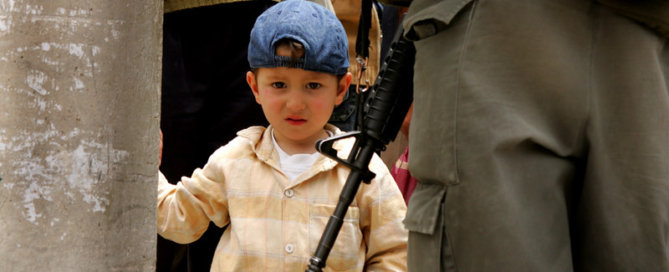 A young child looking scary stands next to a person in uniform holding a weapon