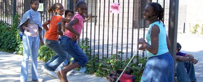 Five girls jump rope on an urban sidewalk