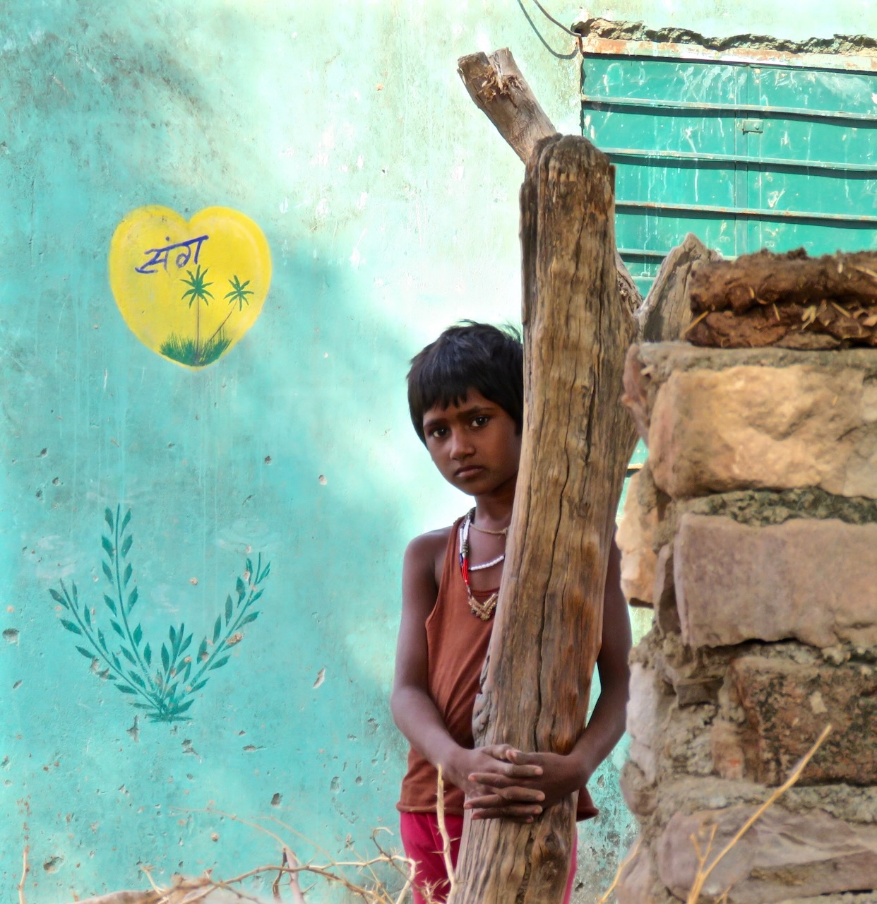 Child holding onto a post in front of a turquoise wall.