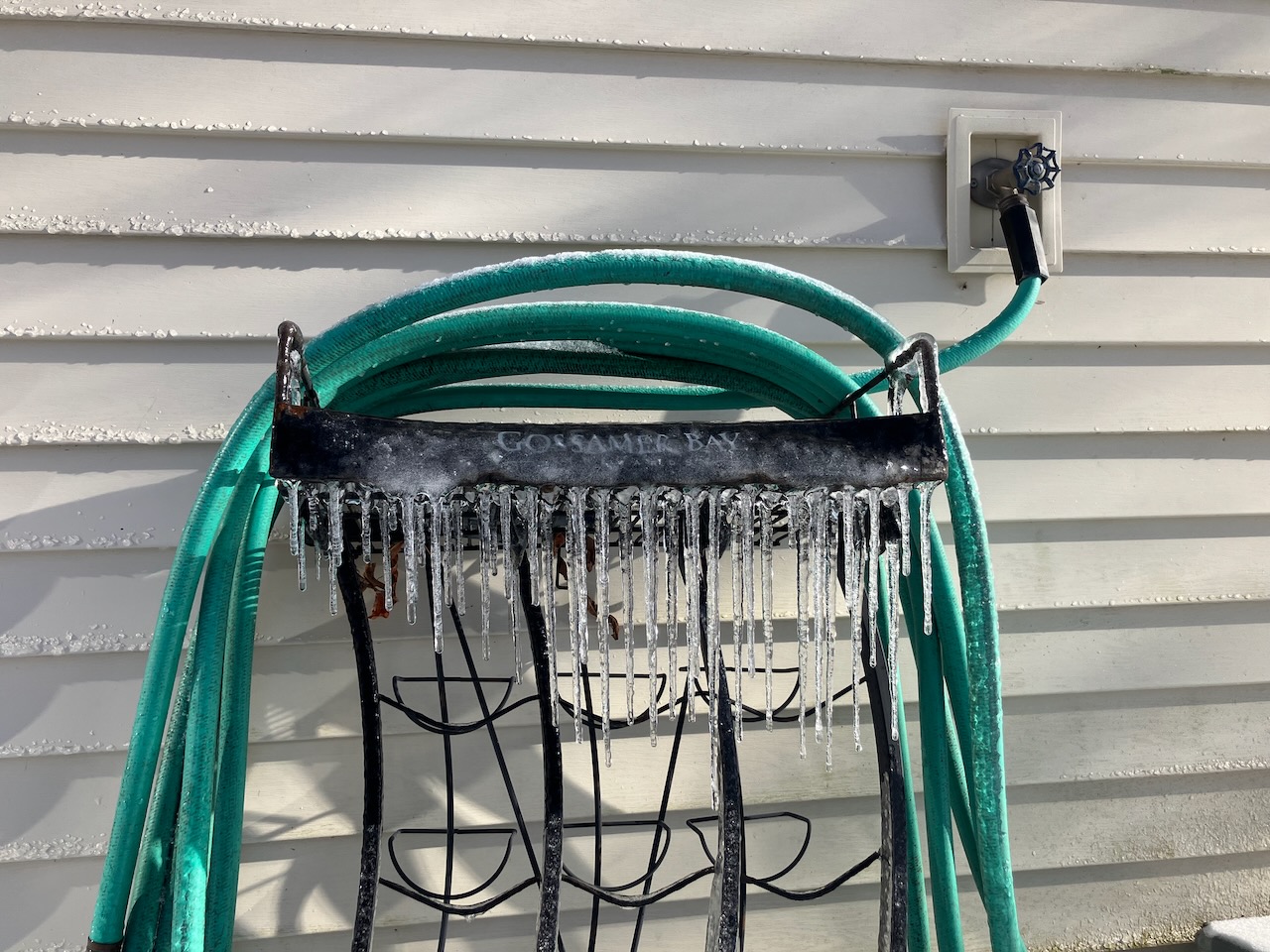 A green garden hose on a rack with icicles